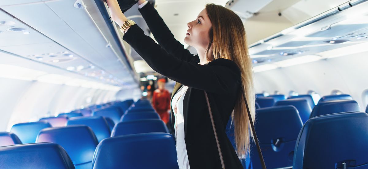 Female student putting her hand luggage into overhead locker on airplane