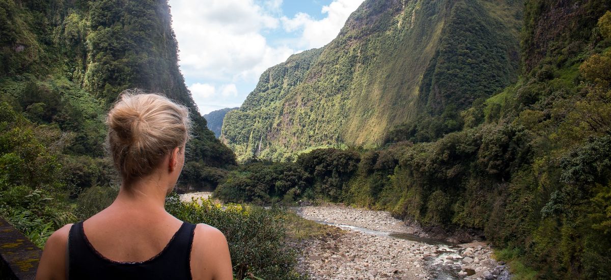 Ile de la Reunion blonde woman looking into a green mountain canyon and riverbed landscape