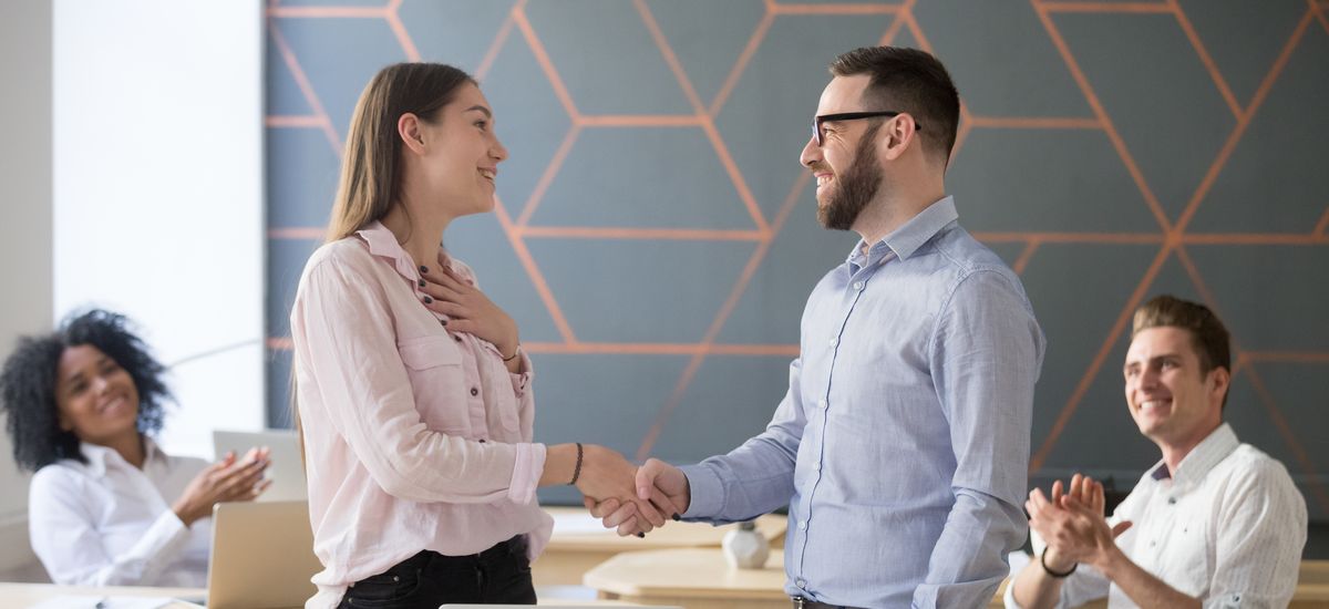 Male boss or team leader shaking hand of female successful employee congratulating with promotion or rewarding, appreciating for good work result  while business team applauding, recognition concept