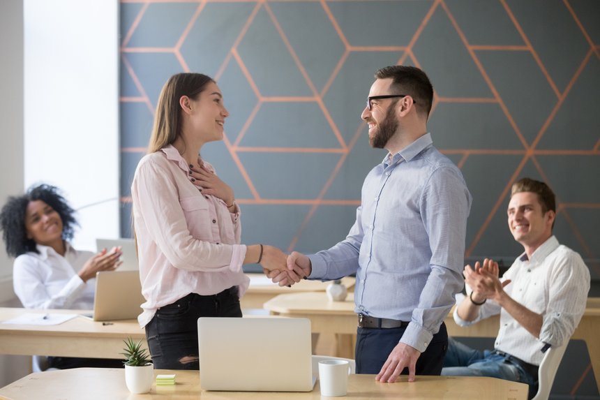 Male boss or team leader shaking hand of female successful employee congratulating with promotion or rewarding, appreciating for good work result  while business team applauding, recognition concept