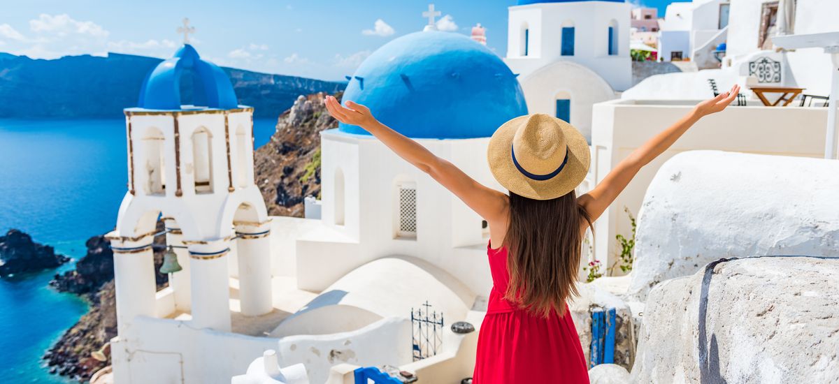 Europe travel happy vacation woman. Girl tourist having fun with open arms in freedom in Santorini cruise holiday, summer european destination. Red dress and hat person.