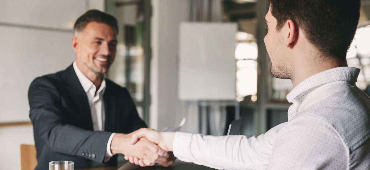 Business, career and placement concept - successful young man smiling, and handshaking with european businessman after successful negotiations or interview in office
