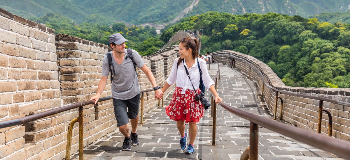 Happy couple tourists holding hands walking up the Great wall of china, top worldwide tourist destination. Young multiracial people travelers during Asia vacation.