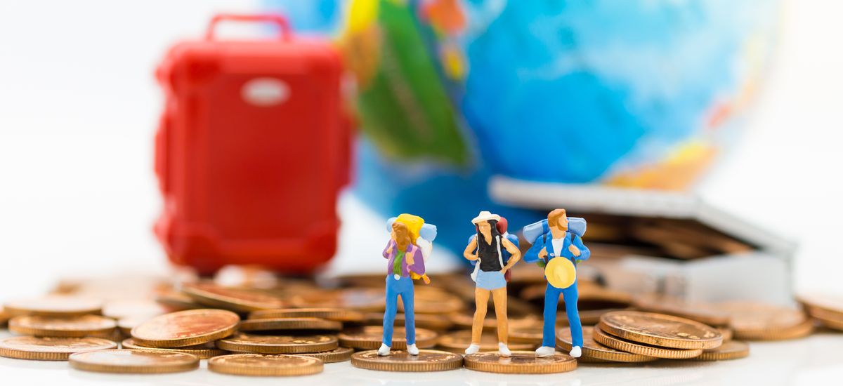 Miniature people : Travelers stand on a pile of coins and have a red suitcase, world map for background. Image use for travel, business concept.