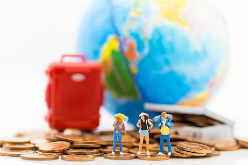 Miniature people : Travelers stand on a pile of coins and have a red suitcase, world map for background. Image use for travel, business concept.
