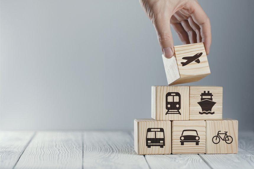 Hand putting a wooden cube with airplane icon on top of cubes with different kinds of transport icons, on neutral background