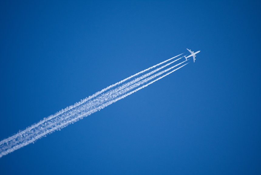 A jet plane flying overhead diagonally with condensation trail.