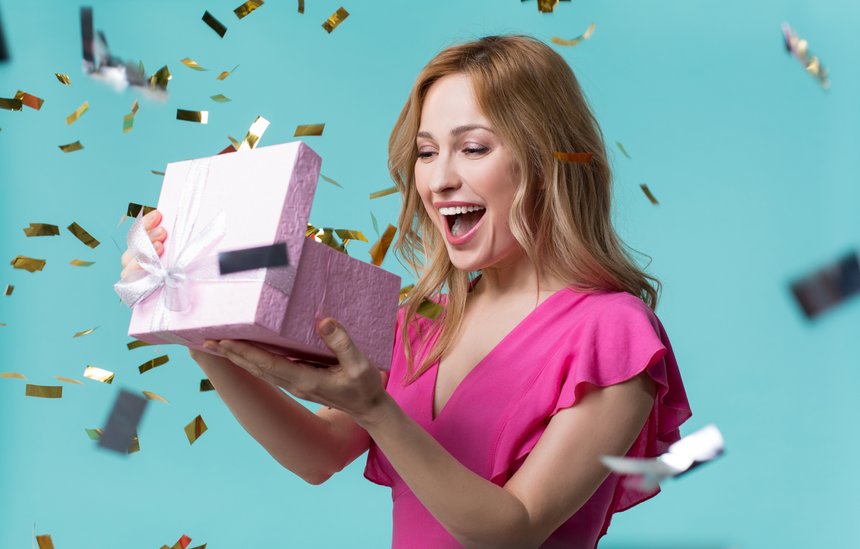 What is inside. Curious young woman is looking into present box and laughing with happiness. Holiday celebration concept