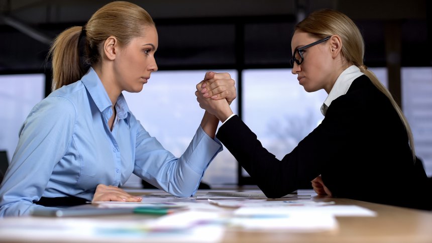 Two businesswomen doing arm wrestling in office, concept of rivalry at work