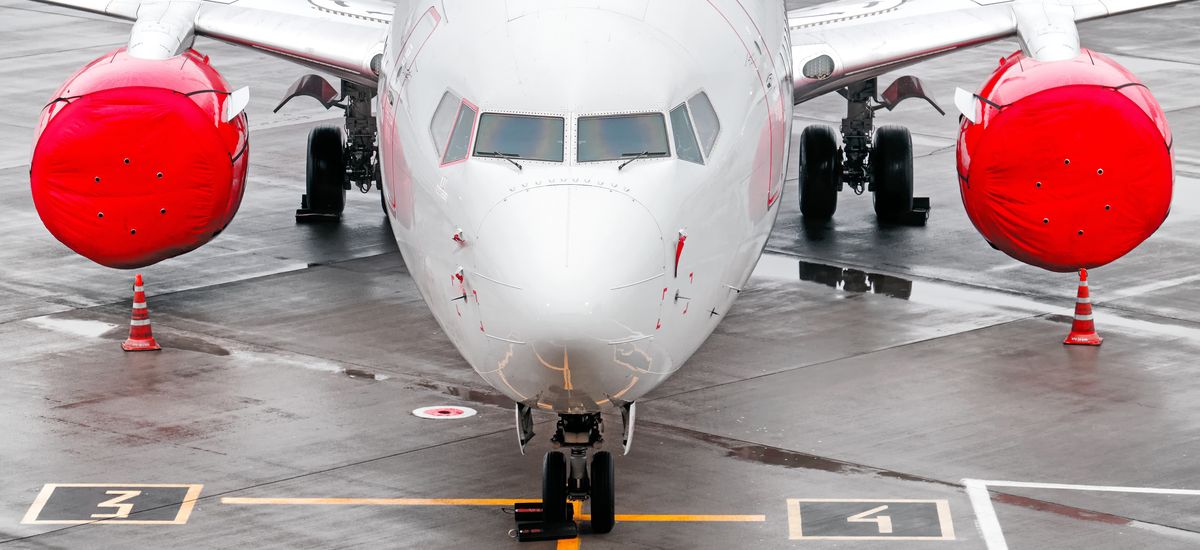 modern airplane on airport runway grounded with red jet plane engine against wet concrete apron background. Aerial top front closeup wide view of passenger aircraft on ground. Air travel banner