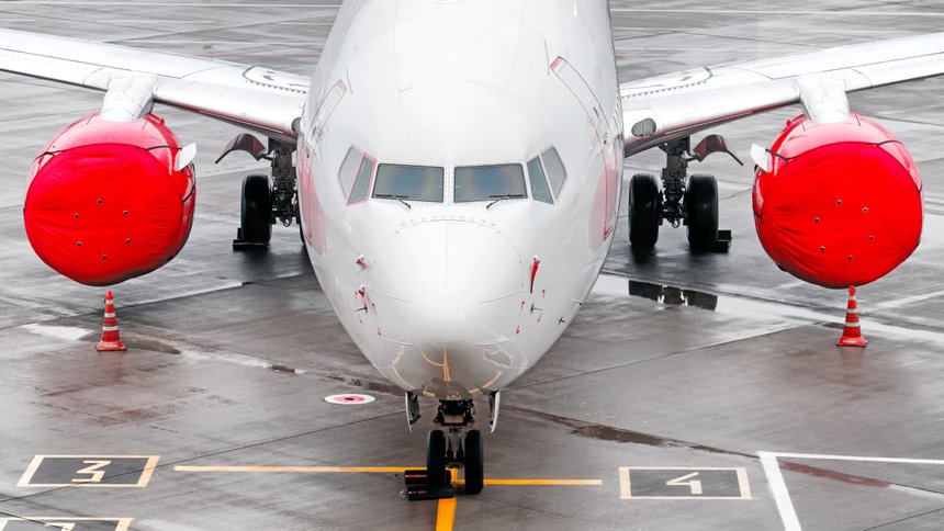 modern airplane on airport runway grounded with red jet plane engine against wet concrete apron background. Aerial top front closeup wide view of passenger aircraft on ground. Air travel banner