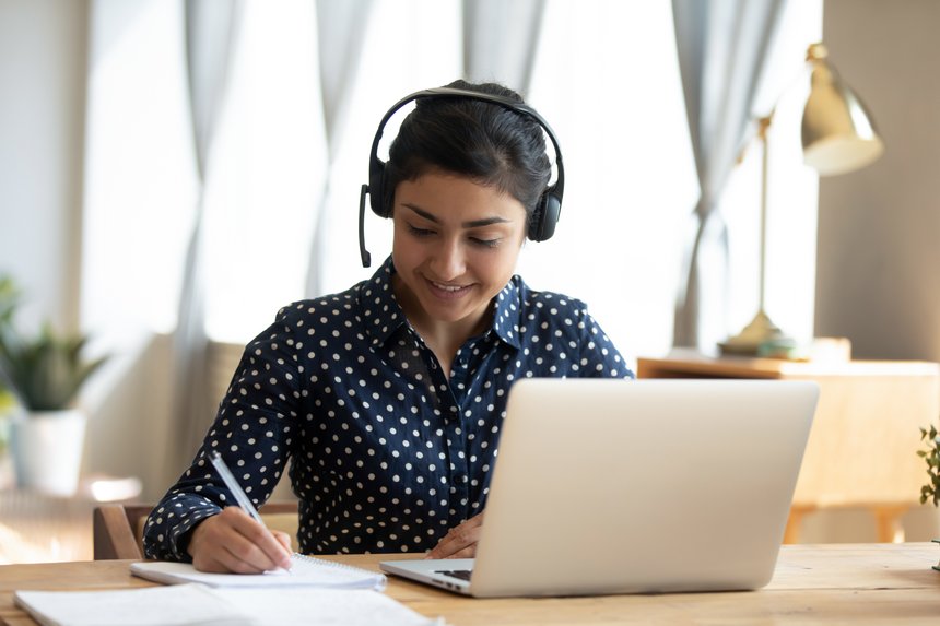 Indian girl student wear headset study online teacher write notes