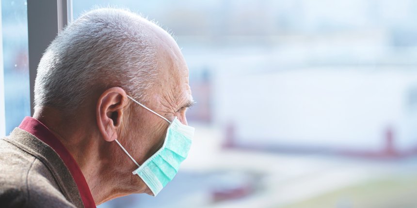 elderly man in protective face mask against virus looks out window stay at home