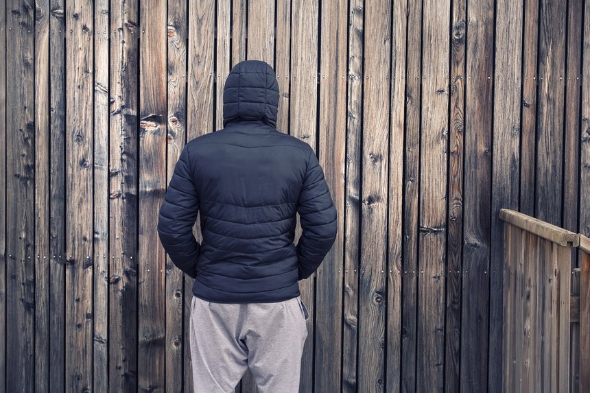 Back view of a young man with a personal problem stands at wooden wall.