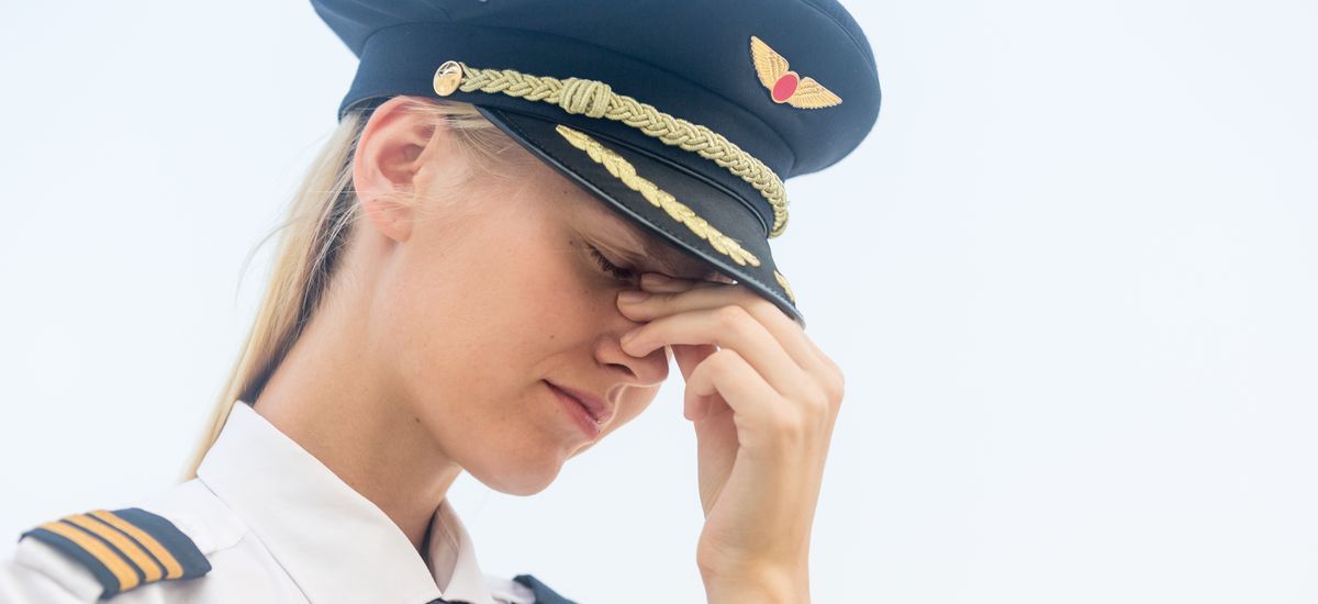 Sleepless tired young female pilot in uniform with her hand on her face. Sad and stressed. Unemployment and depression concept.