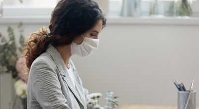 Side view of young businesswoman wearing face mask protects herself from getting flu or coronavirus COVID19 pandemic infectious disease, working typing on computer seated at workplace in office room