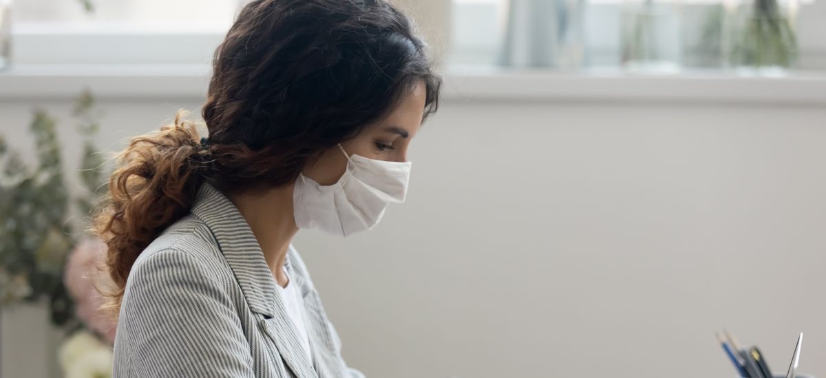 Side view of young businesswoman wearing face mask protects herself from getting flu or coronavirus COVID19 pandemic infectious disease, working typing on computer seated at workplace in office room