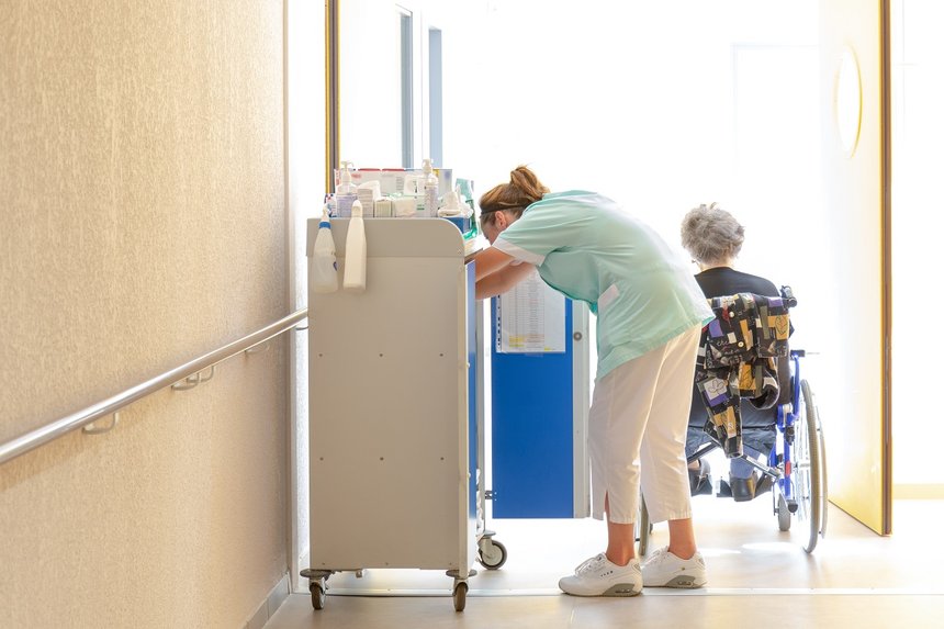 Aide soignante au travail accompagne personne agÃ©e en fauteuil roulant dans couloir hopital clinique maison de retraite