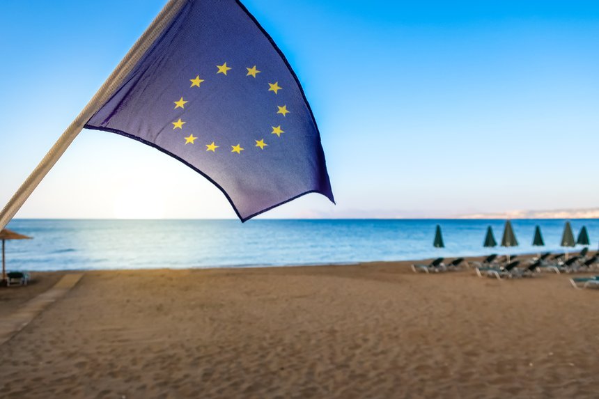 European Union EU flag with beach and sea in the background. Concept for traveling and tourism in Europe.