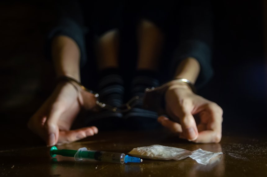 syringe and drugs with a defocused man sitting on the floor and his hands locked in handcuffs.Addict.