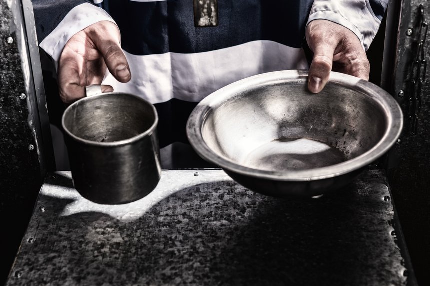 Male prisoner's hands holding aluminum dishes in a hole for supplying food