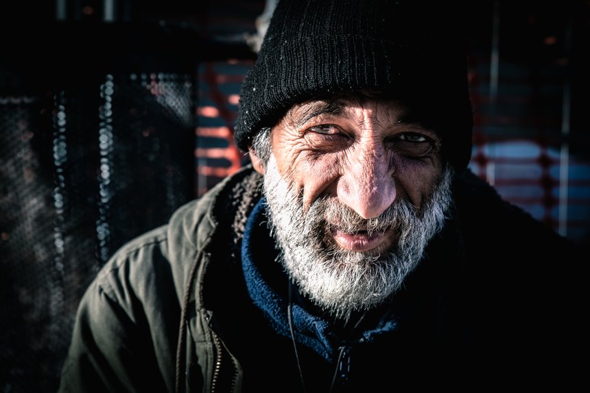 Close up portrait of old smiling homeless alcoholic man face with white beard and hair wandering on the street depressed sick and lonely on cold winter day, social issues documentary concept