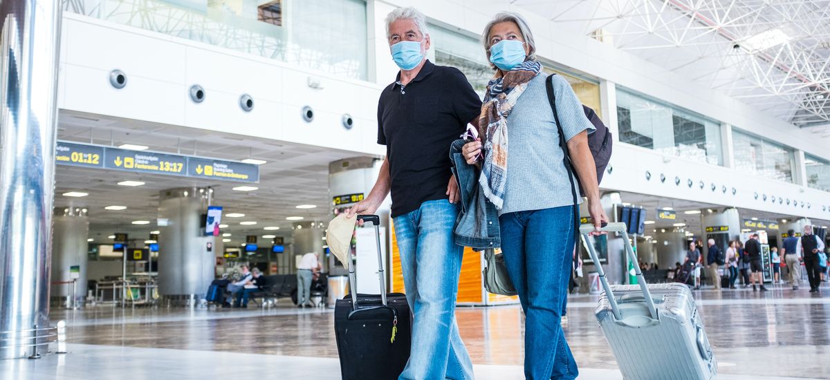 couple of two seniors or mature people walking in the airport going to their gate and take their flight wearing medical mask to prevent virus like coronavirus or covid-19 - carrying luggage or trolley