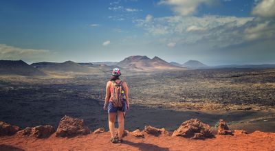 The tourist is standing on the edge of the rock and looks at the red mountains in the national park Timanfaya in Lanzarote