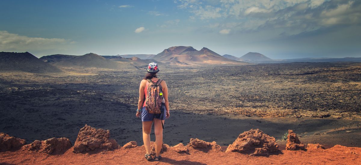 The tourist is standing on the edge of the rock and looks at the red mountains in the national park Timanfaya in Lanzarote