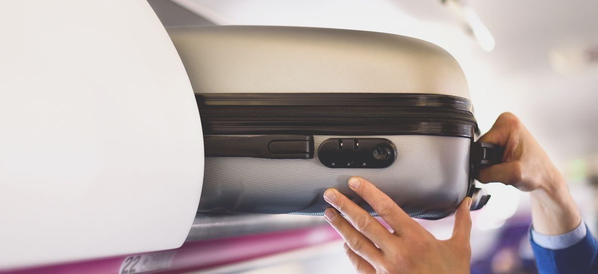 Hand-luggage compartment with suitcases in airplane. Hands take off hand luggage. Passenger put cabin bag cabin on the top shelf. Travel concept with copy space.