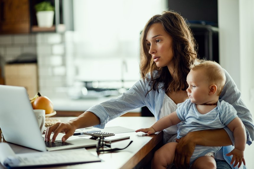 Working mother using laptop while being with baby at home.