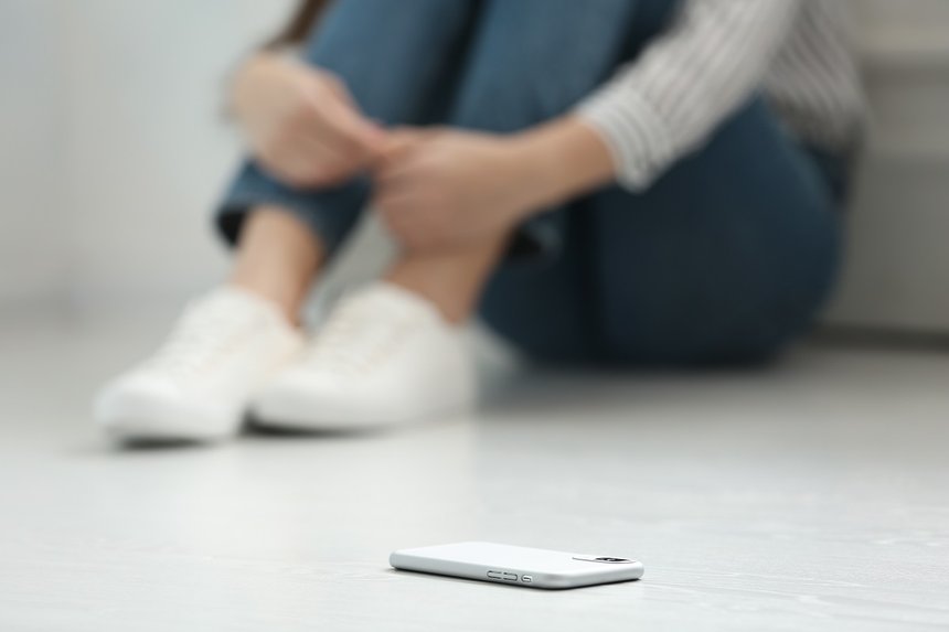 Lonely woman sitting on floor and smartphone on foreground, closeup
