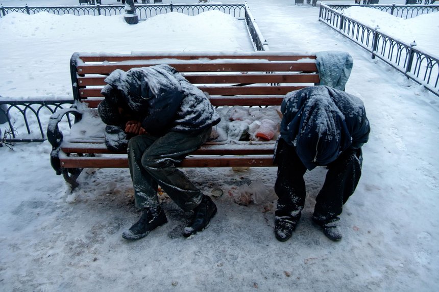 Two unrecognizable dirty homeless men or alcoholics or drug addicts are sleeping on bench in cold winter
