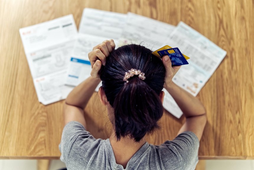 Top view of stressed young sitting Asian woman hands holding the head worry about find money to pay credit card debt and all loan bills. Financial problem concept.