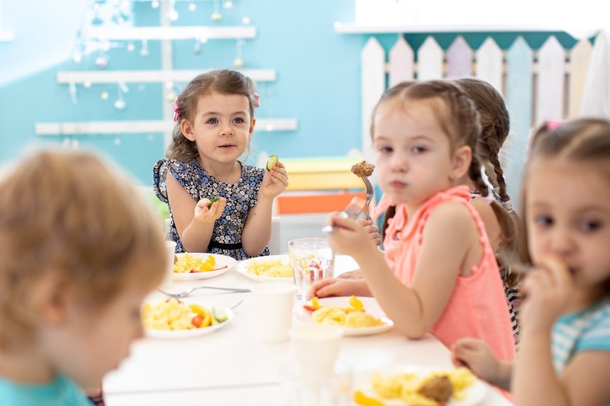 Group of children sitting at the table with lunch and eat appetizing. Kids have a dinner in kindergarten