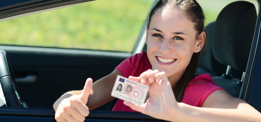 cheerful and happy young woman in her car showing her new drivin