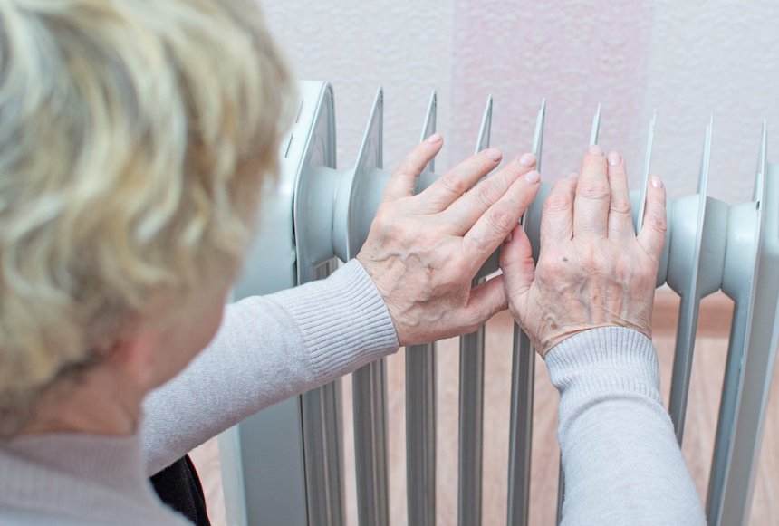 An elderly woman warms her hands on the radiator. Energy crisis,