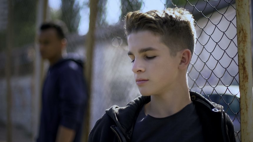 Teenage boys leaning on metal fence, juvenile detention center, 