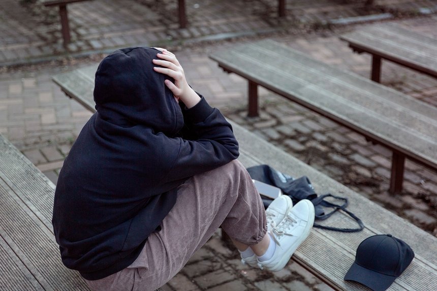 A teenage girl in a black hoodie with a hood on her head is sitt