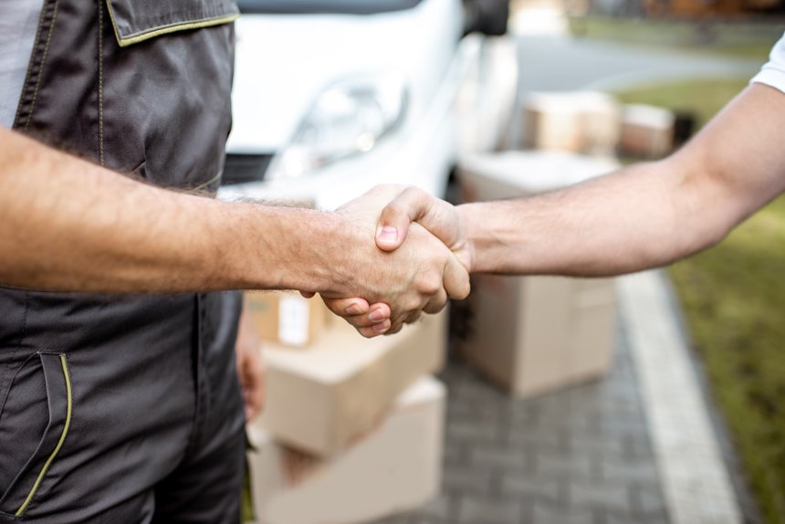Delivery men shaking hands with a client while delivering goods outdoors, close-up on hands