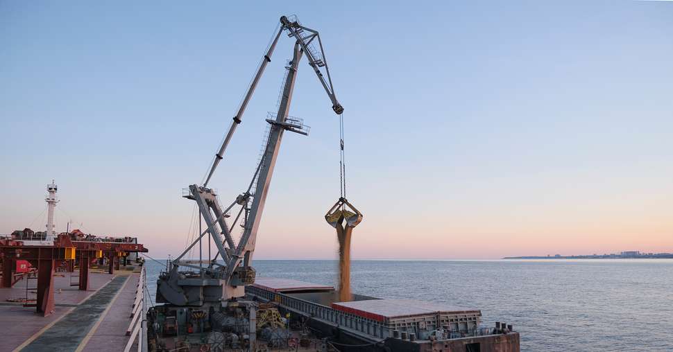 Transshipment of grain products from bulk carrier to the barge on Odessa, Ukraine anchorage during sunset