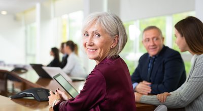 Side view portrait of friendly smiling classy gray-haired senior white businesswoman sitting at table during corporate team meeting in conference room