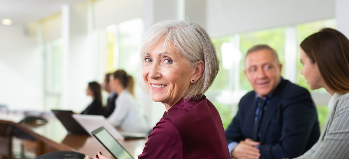 Side view portrait of friendly smiling classy gray-haired senior white businesswoman sitting at table during corporate team meeting in conference room