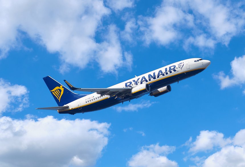 Ryanair plane flying on a beautiful blue sky with scattered clouds, with airline logo clearly readable in full.