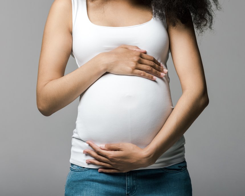 cheerful pregnant african american girl touching belly on grey