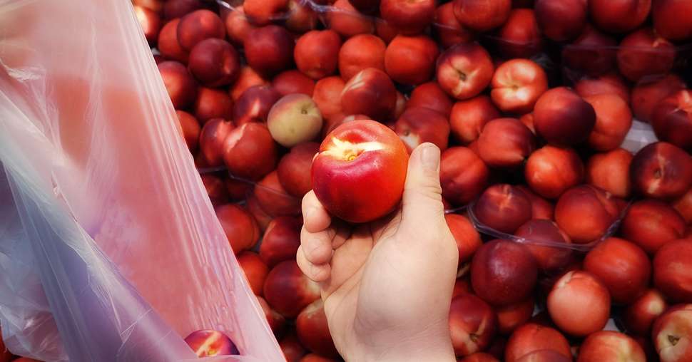 Hand with nectarine. At the Grocery Store. Choosing a nektarine.