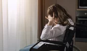 Pensive disabled woman with infantile cerebral paralysis sits in wheelchair near window behind curtain at home experiencing ableism, sunlight.