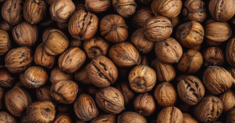 A close-up of a pile of raw, natural walnuts with their shells still intact.