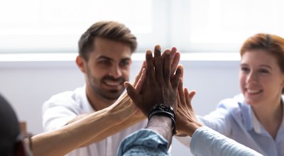 Happy diverse businesspeople giving high five, close up focus on people hands. Friendly multiracial company staff stacked their palms together symbol of friendship and good relations between coworkers