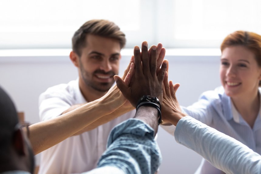 Happy diverse businesspeople giving high five, close up focus on people hands. Friendly multiracial company staff stacked their palms together symbol of friendship and good relations between coworkers